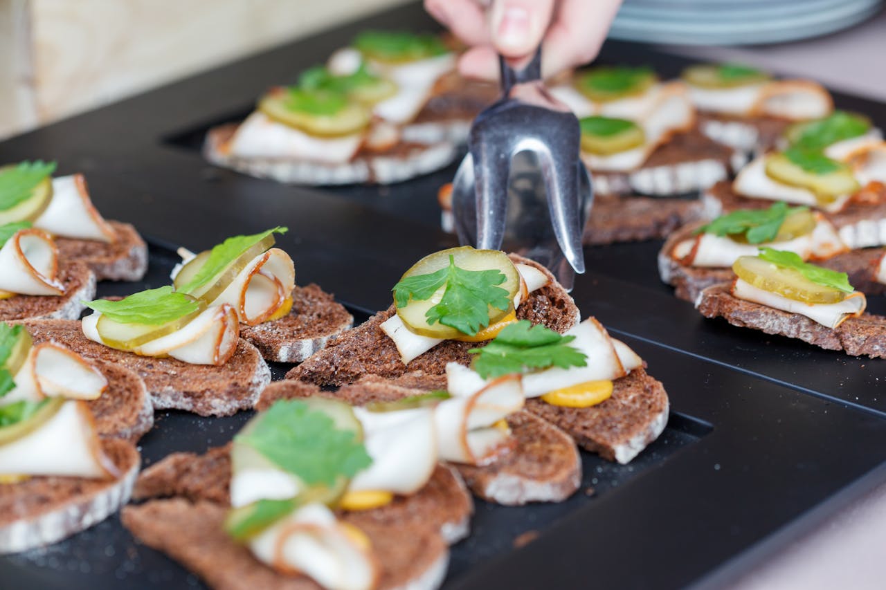 High angle of crop anonymous person with tongs taking delicious sandwich made of rye bread lard with pickled cucumber and sprig of parsley